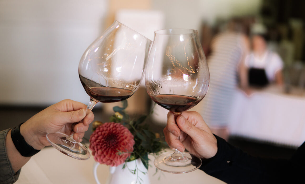 Two hands holding glasses of wine, toasting each other.