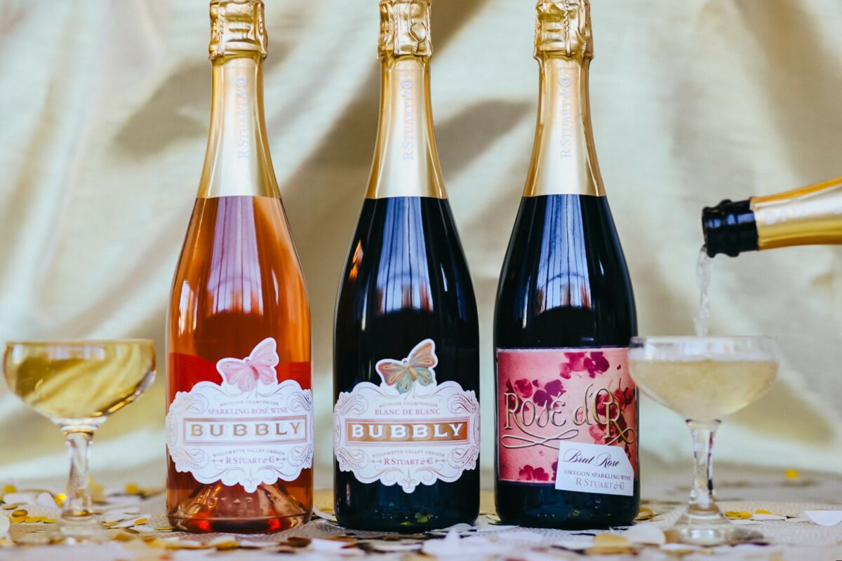Three bottles of sparkling wine with two glasses being filled
