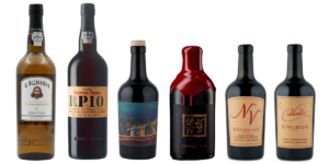 An image of the 6 bottles lined up next to each other, showcasing the port wines tasted. From left to right, the bottles are: Ramos Pinto white port, Ramos Pinto 10 Year Tawny, Coelho NV Dessert Wine Aventure, Dominio IV Unraveling Rubies Fortified Wine, R. Stuart NV Tawny, and R. Stuart 2013 Colheita.